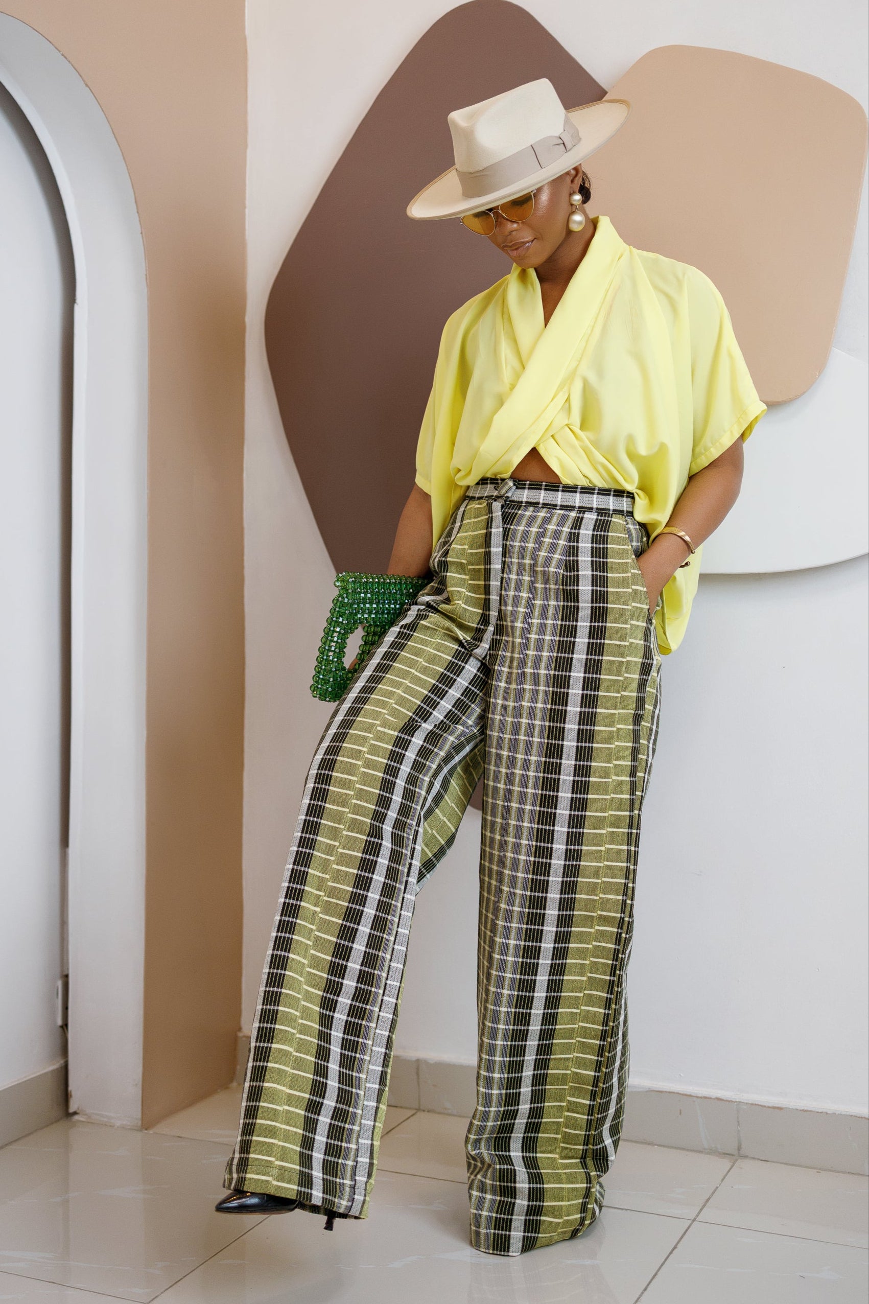 Model wearing Akudunufe set – yellow soft crepe top with Aso Oke striped wide-leg trousers, accessorized with hat and beaded bag.