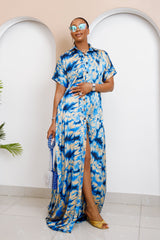 Woman wearing a blue patterned dress standing in a room with arches and a plant.