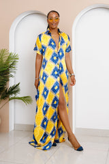 Woman wearing a yellow and blue patterned dress standing in a room with arches and a plant.