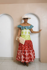 Model wearing Enenia off-shoulder boho-style Adire dress with ruffled neckline, fitted bodice, and flowy red and green patterned skirt.