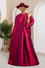 Woman in a burgundy Micado caftan with pearl embellishments, exuding elegance.