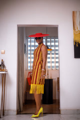 A woman posing in a red and yellow African Ankara print midi dress with frills at the bottom.