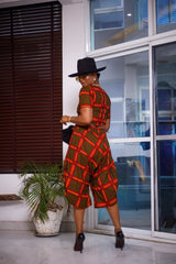 A woman posing in a yellow black and red two-piece set. She is pictured with her back to the camera and looking over her shoulder. She is styled with a black sun hat and silver jewelry.