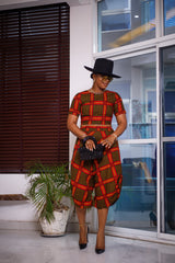 A woman posing in a yellow black and red two-piece set. She is pictured facing the camera and looking down. She is styled with a black sun hat and silver jewelry.