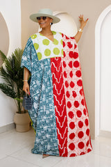 Woman wearing a vibrant, hand-dyed Adire kaftan with geometric and polka dot patterns in blue, red, and green, styled with a chic hat and accessories.