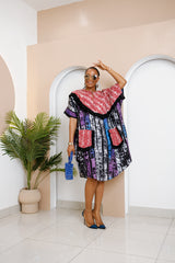 Model wearing Nwayiocha Adire Midi Dress in black, purple, and blue stripes with red patterned yoke and pockets trimmed with black fringe, holding blue beaded bag.