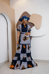 Model wearing Nzama Ankara maxi shirt dress with patchwork print in indigo, white, and orange, styled with a wide-brimmed hat and accessories.