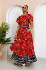 Model wearing red Obataobie Ankara Maxi Dress with flutter sleeves and black-and-white hem, standing confidently in a minimalist indoor space.