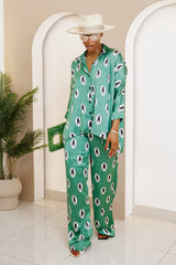 Woman wearing a stylish green silk co-ord set with a modern African print, oversized button-down shirt, and wide-leg pants, accessorized with a hat and bag.